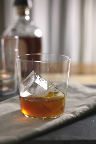 Low ball cocktail glass with bourbon, honey and ginger ale. Cocktail shaker in background