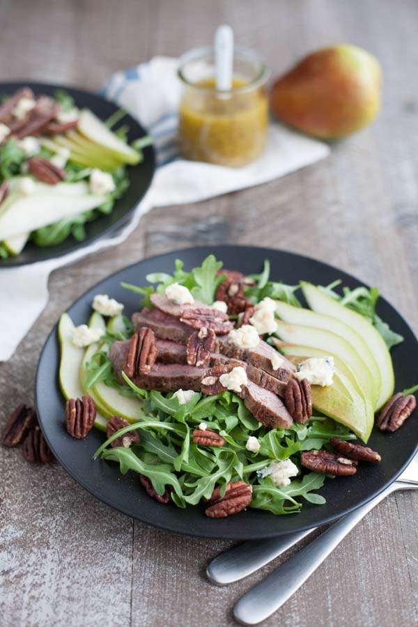 Arugula Flank Steak Salad with Pears and Blue Cheese | BourbonandHoney.com -- Filling, savory and delicious, this Flank Steak Salad recipe is topped with fresh pears, toasted pecans and lots of blue cheese and perfect for lunch or dinner!