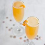 Two champagne glasses filled with a Bourbon and Honey French 75 Cocktail. On a marble counter with gold confetti.