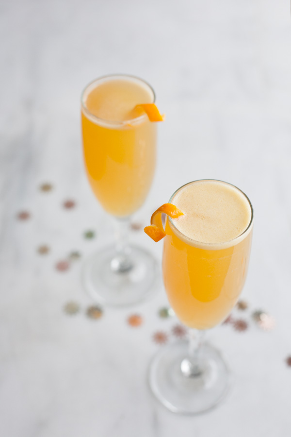 Two champagne glasses filled with a Bourbon and Honey French 75 Cocktail. On a marble counter with gold confetti.