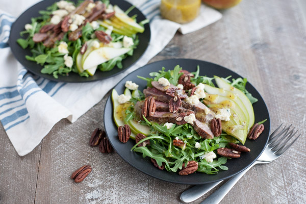 Arugula Flank Steak Salad with Pears and Blue Cheese | BourbonandHoney.com -- Filling, savory and delicious, this Flank Steak Salad recipe is topped with fresh pears, toasted pecans and lots of blue cheese and perfect for lunch or dinner!